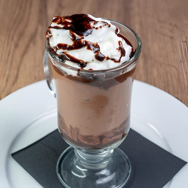 Rich chocolate mousse dessert in a glass, topped with whipped cream and chocolate drizzle.