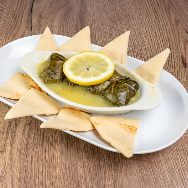 Dolmades, grape leaves stuffed with rice, served in a white dish with lemon and pita bread.