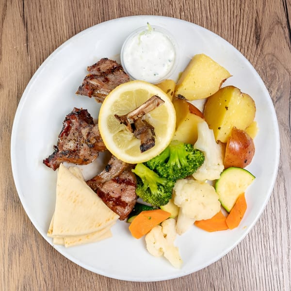 Grilled lamb chops with roasted potatoes, steamed vegetables, pita bread, and a side of tzatziki.